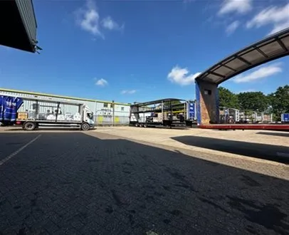 Wide view of a logistics yard with multiple open curtain-side trailers being loaded under clear blue skies, showcasing active freight distribution.